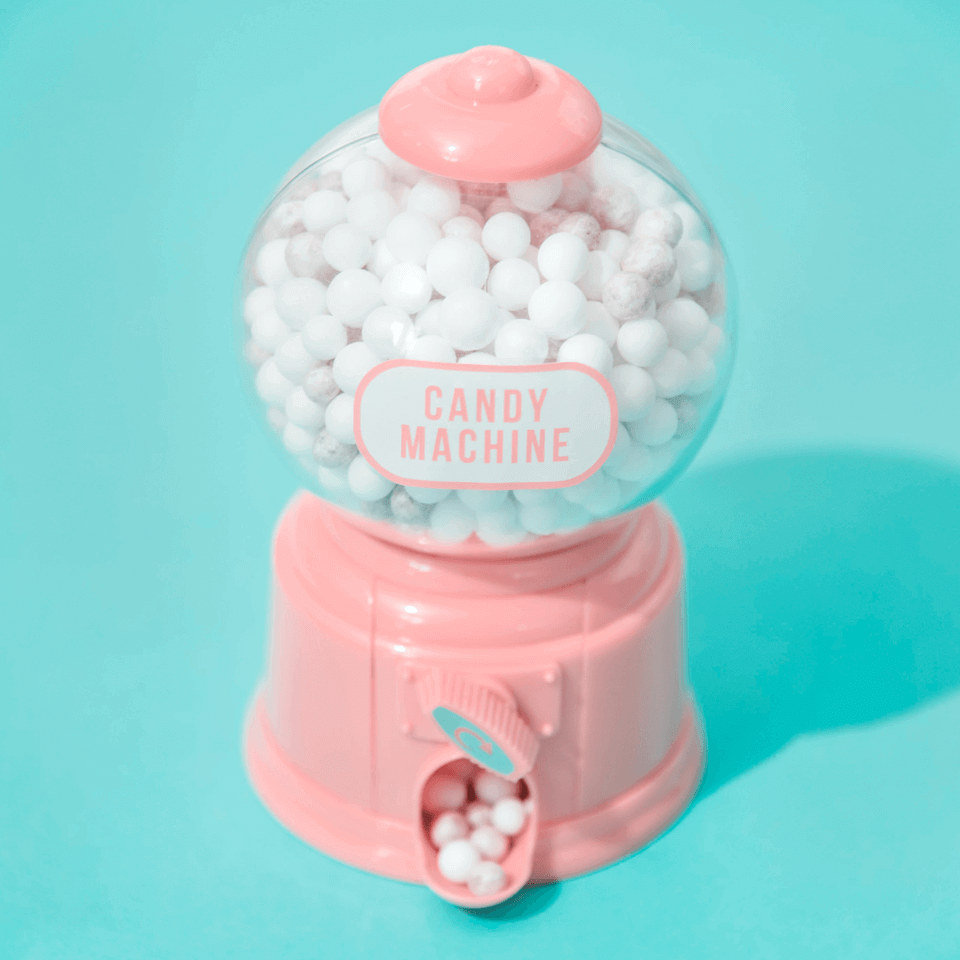 A soft pink machine that dispenses white candy balls on a light blue background.