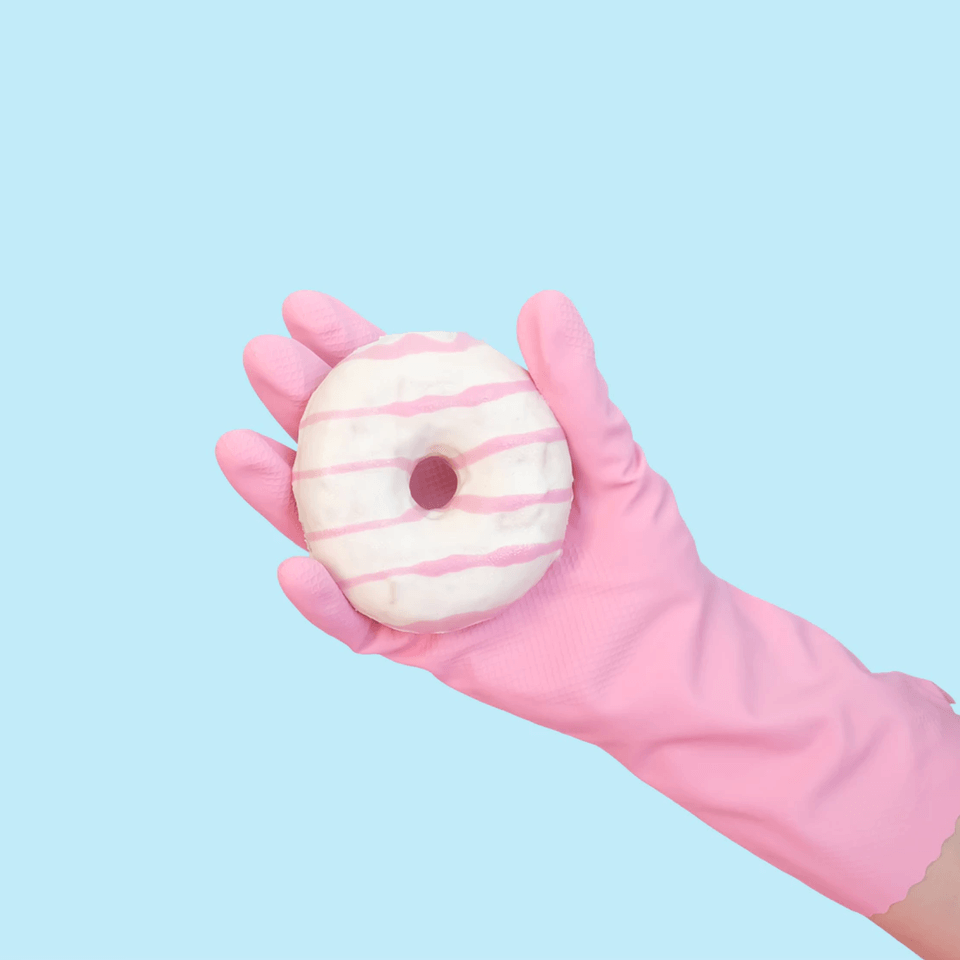 A hand with a pink rubber glove holding a white and pink striped donut.